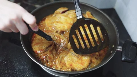Close-up of marinated pork steaks cooking in savory sauce in a frying pan o.. Видео 340635878
