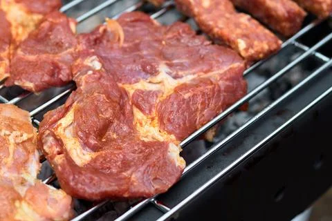 Close-up of marinated raw meat steaks grilling on a charcoal barbecue grid Stock Photos