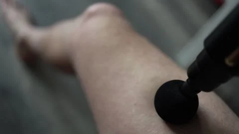 Close-up of a massage gun being used on a person's leg to relieve muscle tension Stock Footage 303908327