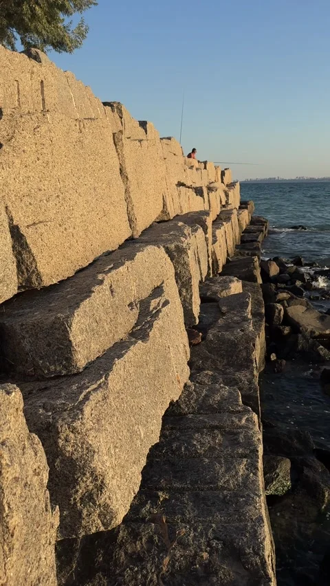 Close up of a massive stone block breakwater wall on the coast bathed in warm Stock Footage 341464447