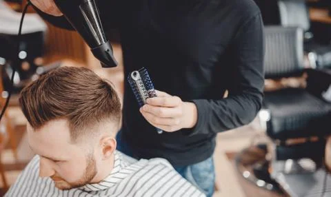 Close-up master Barber does hairstyle and styling with dryer hair to guy Stock Photos