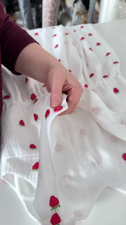 In close-up, the master carefully sews a red button on the dress with white Stock Footage 296074633