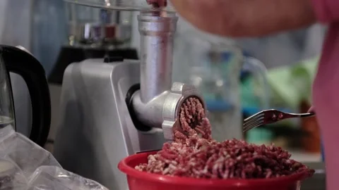 A close-up of a meat grinder producing fresh ground meat, with a hand guiding Stockbeeldmateriaal 308925649