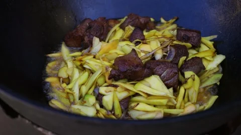 Close-up of meat, onion and sliced carrots frying in hot oil in a large cauldron Stock Footage 333037588