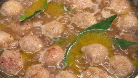 Close-up of meatballs simmering in bubbling broth or sauce with bay leaves,.. Stock Footage 327955990