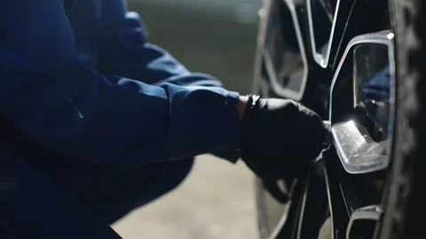 Close-up of a mechanic in blue coveralls using a wrench to tighten lug nuts on a Video stock 333839453