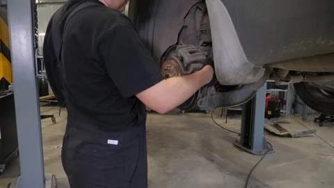 Close-up of a mechanic replacing brake pads on a car wheel at a service station. Stock Footage 339787214