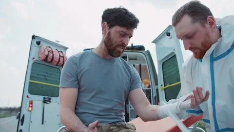 Close up medic provides first aid and rewinds his hand with a bandage to wounded Stock Footage 187722935