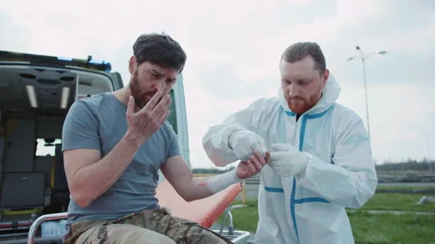 Close up medic provides first aid and rewinds his hand with a bandage to wounded Stock Footage 195521953