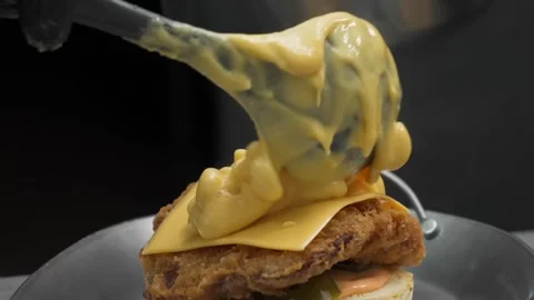 Close-up of Melted Cheddar Cheese Sauce Poured Over a Crispy Fried Chicken Sandw Stock Footage 331633984