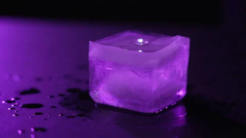 Close-up of a melted ice cube on dark background with purple lighting Stock Footage 168943946