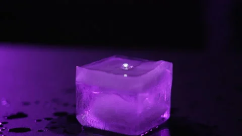 Close-up of a melted ice cube on dark background with purple lighting Stock Footage 168966587