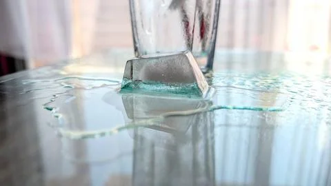 Close Up Of A Melting Ice Cube On A Reflective Glass Table With Sweating Gl.. 库存照片