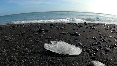 Close-up of a melting ice diamond on a volcanic shore with ocean waves Stock Footage 334047245