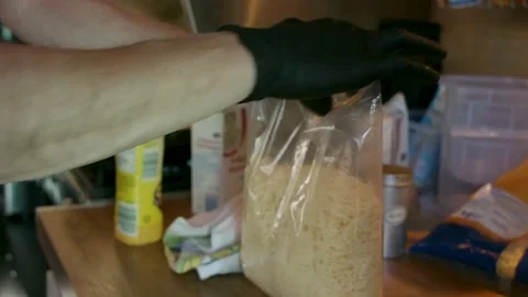 Close up men opens cheese bag with a knife and pours it in a pan with pasta Stock Footage 203891450