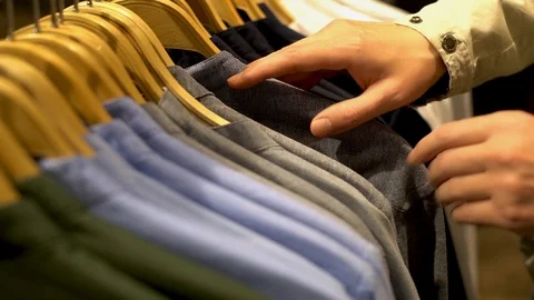 Close-up of men's hands on a clothes rack hanger choosing a modern shirt in a tr Stock Footage 120071346