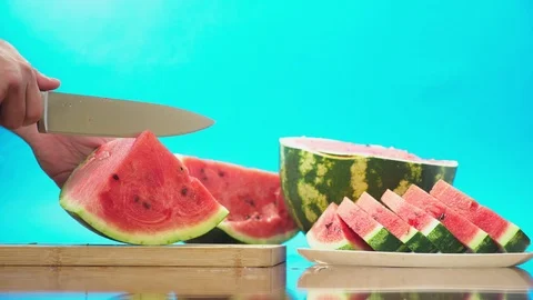 Close-up. Men's hands cut the watermelon into pieces. Blue background. Stock Footage 95355144