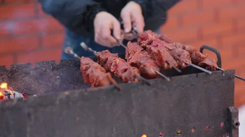 Close up of men's hands placing shashlik on the grill. Barbecue meat on skewers Stock Footage 132696830