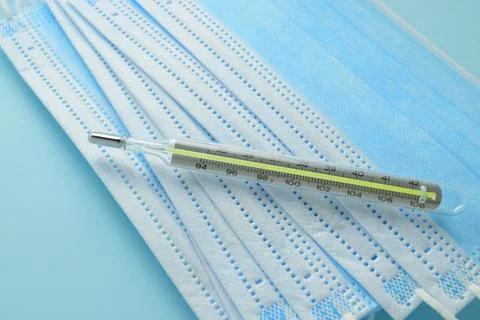 Close-up of a mercury thermometer and a stack of blue medical masks Stock Photos