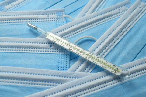 Close-up of a mercury thermometer and a stack of blue medical masks Stock Photos
