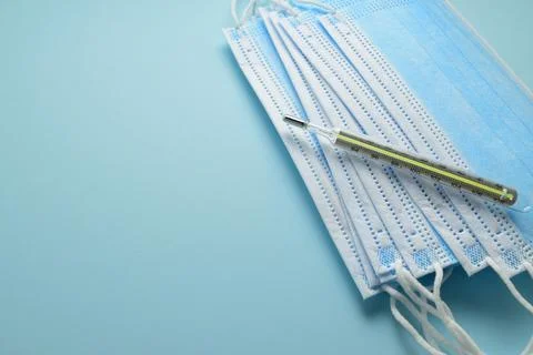 Close-up of a mercury thermometer and a stack of blue medical masks Stock Photos