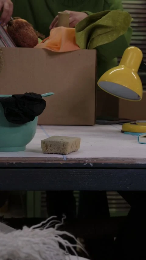 Close-up of a messy creative workspace with craft supplies, fabrics, lamp, and t Stock Footage 328605041