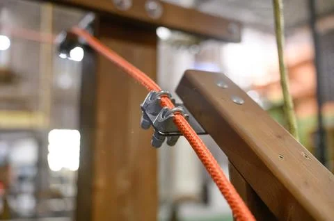Close-up of metal clamp securing red rope on wooden structure indoors Stock Photos