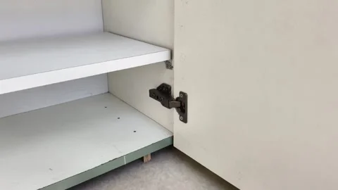 Close up of a metal concealed hinge installed on a white wooden cupboard door Видео 325319304