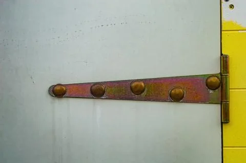 Close up of a metal hinge with five rivets securing a gray door to a yellow.. Foto stock