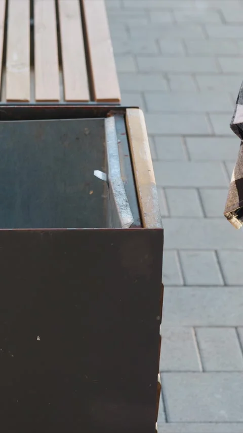 Close up of metal trash bin with litter inside on gray brick pavement next to Stock Footage 345063393