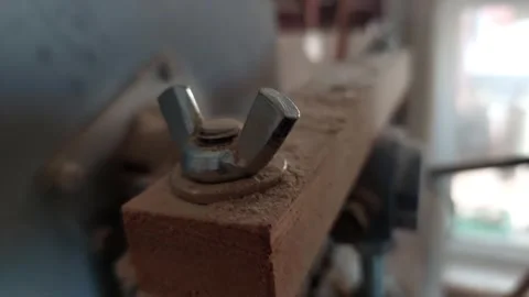Close-up of a metal wing nut on a dusty wooden machine in a workshop Stock Footage 335644433