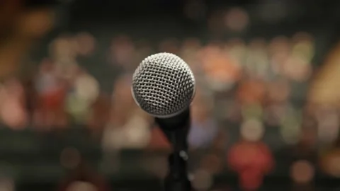 Close up of microphone in full theatre with blurry crowd Stockbeeldmateriaal 221581642