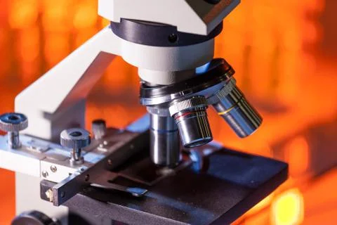 Close up of microscope lenses focused on a specimen in warm orange light light. Stock Photos