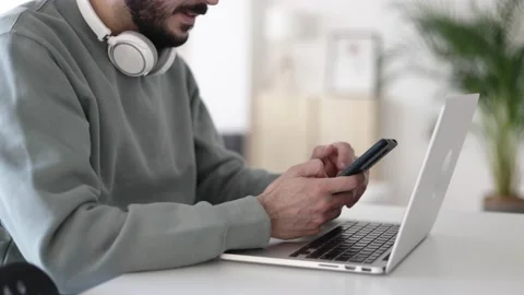 Close up mid adult man using cell phone while working on laptop at home Stock Footage 168842314