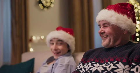 Close-up of middle-aged man and teenager sitting on sofa laughing out loud. They Видео 210619598
