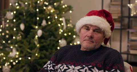 Close-up of middle-aged man sitting by Christmas tree and looking away. He is 動画素材 210564112