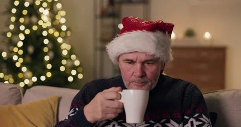 Close-up of middle-aged man sitting on sofa and wearing Santa hat. The man took Stockbeeldmateriaal 210634351