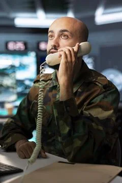 Close up of military operator using landline phone while seated at computer desk Stock Photos