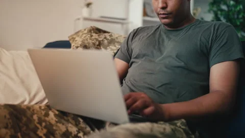 Close-up of military typing on laptop while sitting on sofa at home, remote work Video stock 258282120