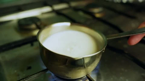 Close-up of milk being placed on a gas burner in a metal saucepan, blue flame Stock Footage 331108841