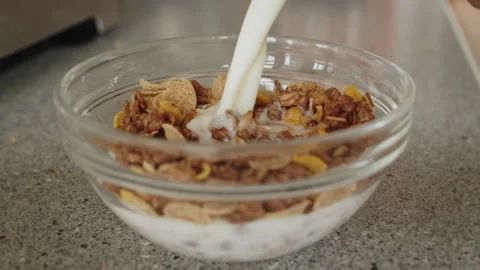 Close up of milk slowly getting poured into a glass bowl with cereal in it. Stock Footage 168354587