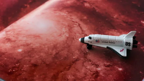 Close up of a miniature toy space shuttle placed on a reddish galaxy background Stock Footage 316646515