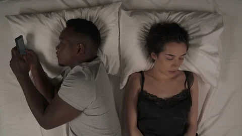 Close-up of mixed-race couple in bed at night. White woman telling something to Stock Footage 136577449