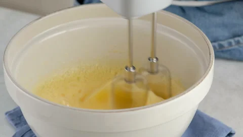 Close-up mixing egg whites, yolks and sugar in a ceramic bowl with a hand mixer Stock Footage 148568751