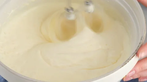 Close-up mixing egg whites, yolks and sugar in a ceramic bowl with a hand mixer Stock Footage 148569175