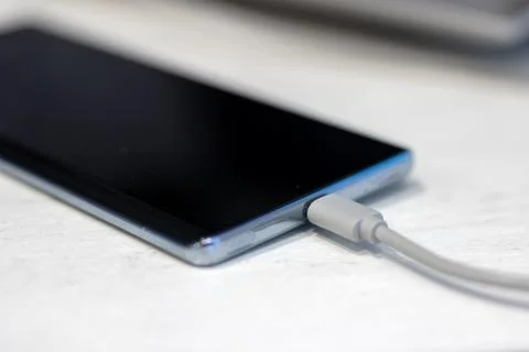Close up of mobile device charging on clean desk with gentle daylight reflection Stock Photos