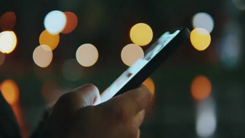 Close-up of a mobile phone in hands on a dark background with bokeh Video stock 242626597