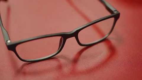 Close-up of modern black rectangular reading glasses placed on a vibrant re.. 動画素材 336531375