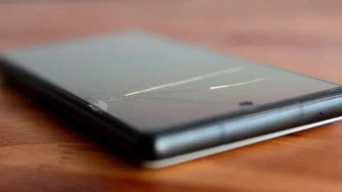 Close-up of a modern smartphone with a severely cracked screen on a wooden .. Stock Footage 342501027