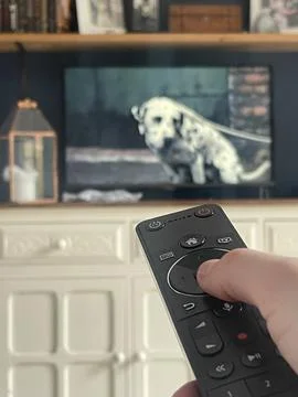 Close up of a modern tv remote control in the hand of a viewer, tv on backgro Stock Photos